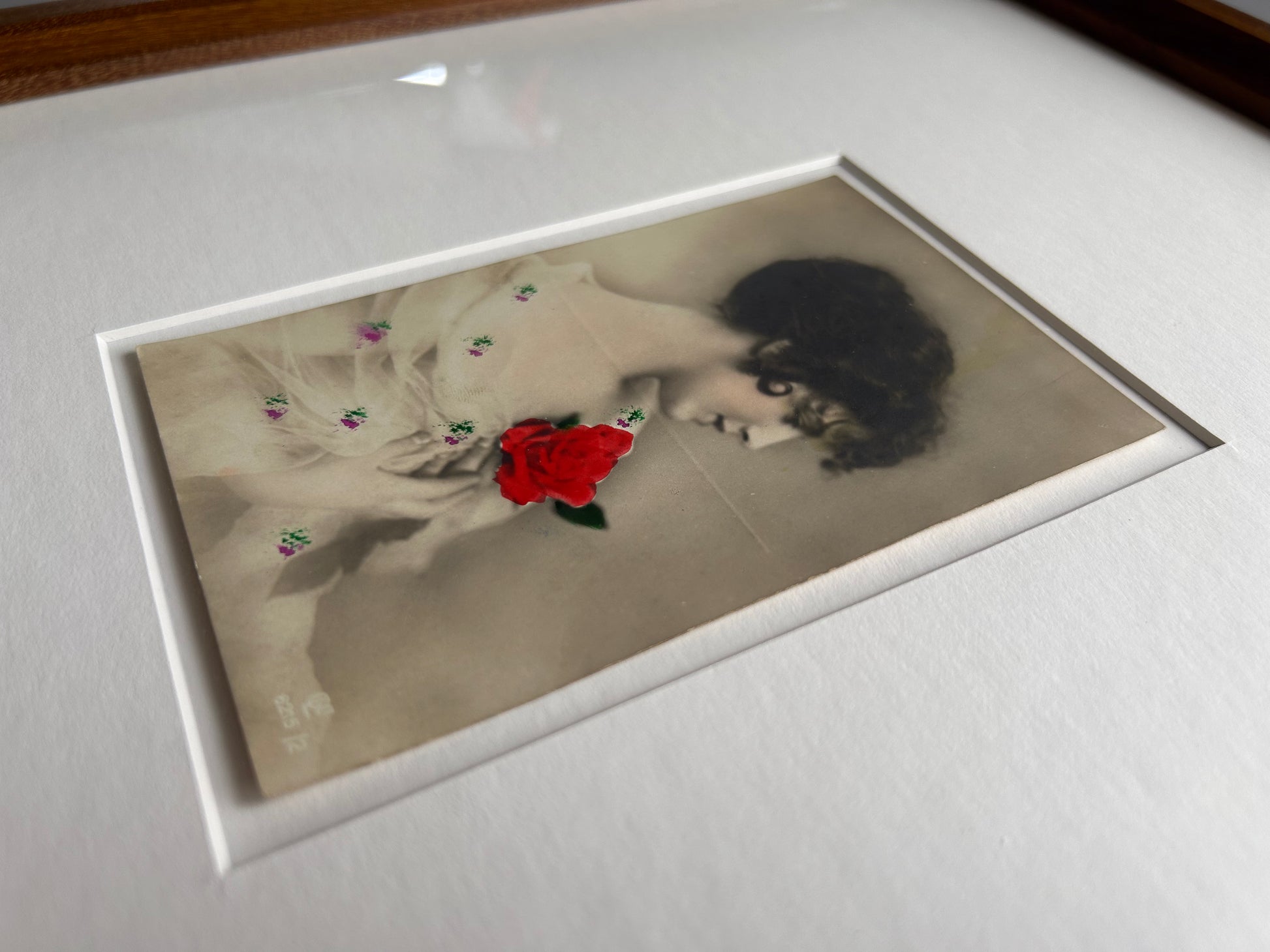 By any other name - Framed 1920s Hand-Colored Postcard featuring a soft portrait of a woman holding a flower – Vintage Parisian Portrait in Merbau wood Frame
