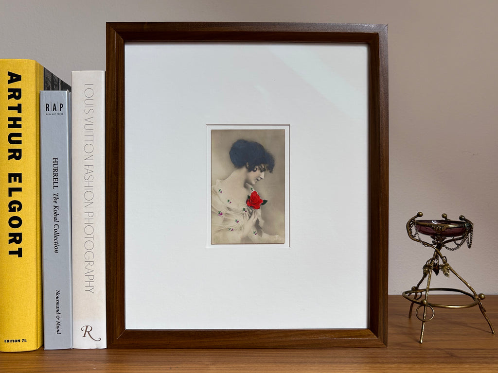 By any other name - Framed 1920s Hand-Colored Postcard featuring a soft portrait of a woman holding a flower – Vintage Parisian Portrait in Merbau wood Frame
