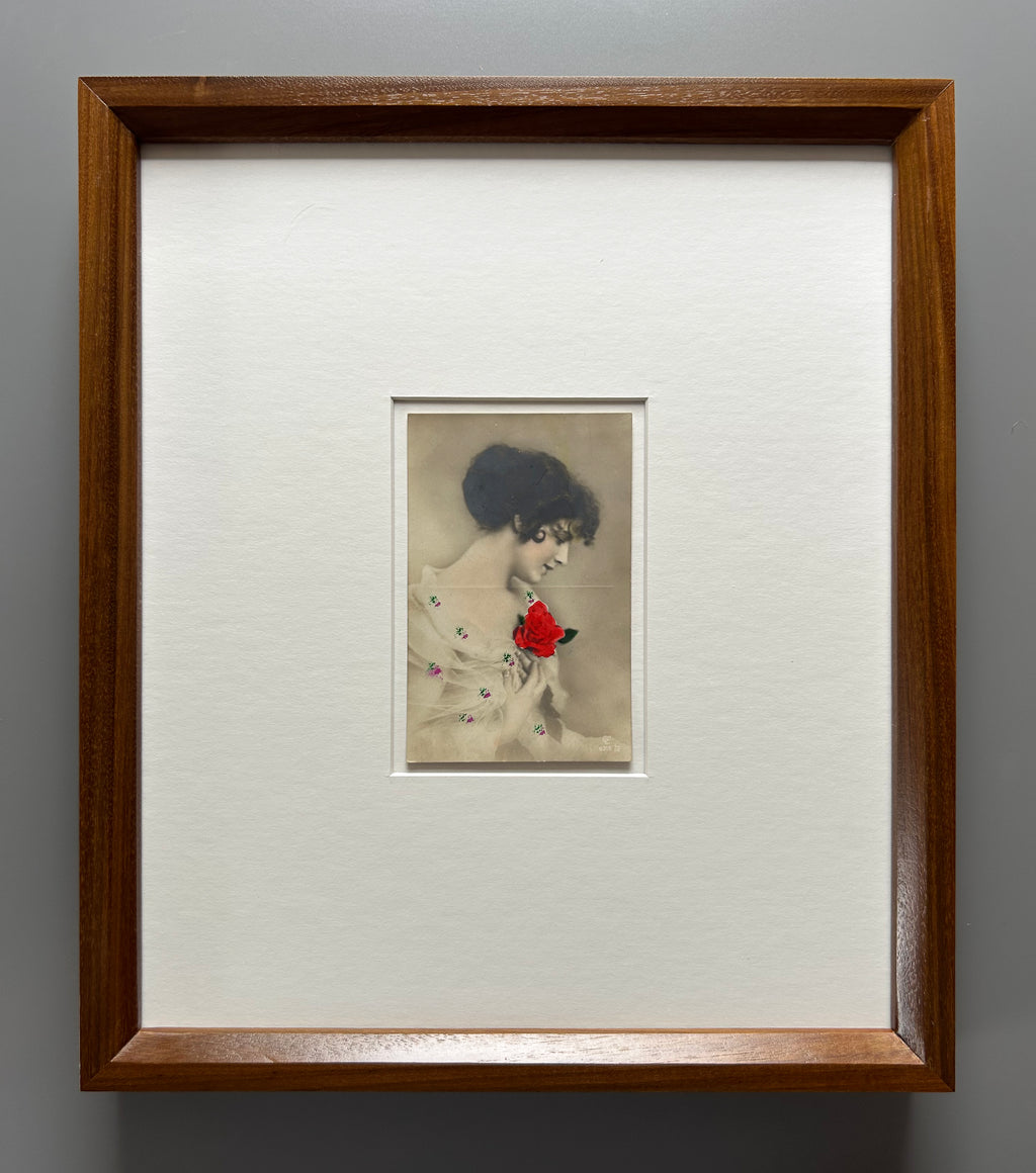 By any other name - Framed 1920s Hand-Colored Postcard featuring a soft portrait of a woman holding a flower – Vintage Parisian Portrait in Merbau wood Frame