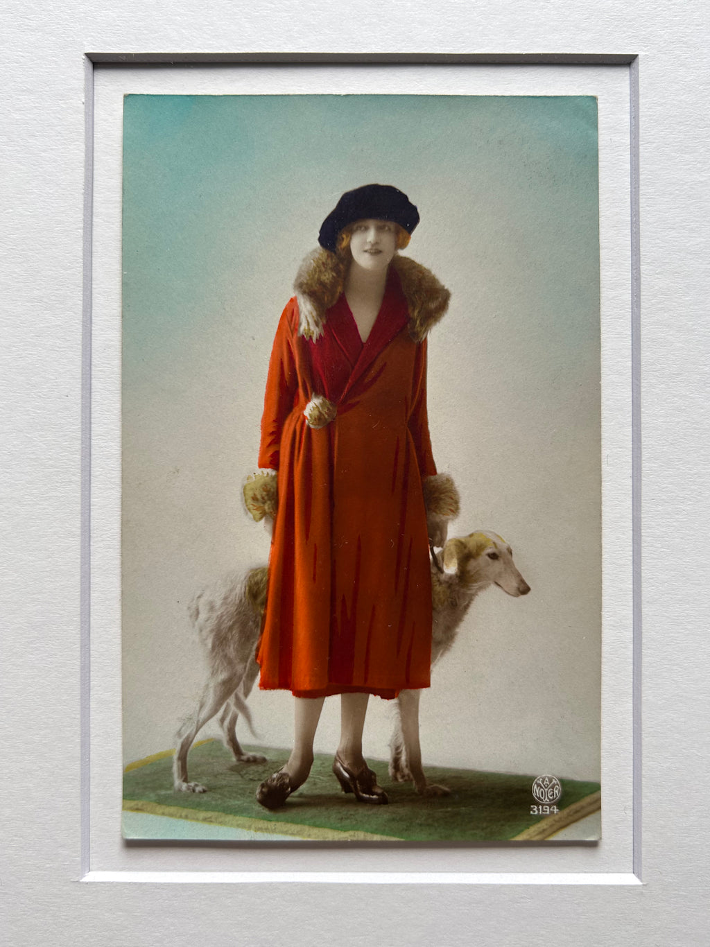 Framed 1920s Fashion Postcard with a poised female model in a fur-trimmed orange coat and black beret, standing confidently beside a Borzoi dog in a handmade Jatoba Wood Frame