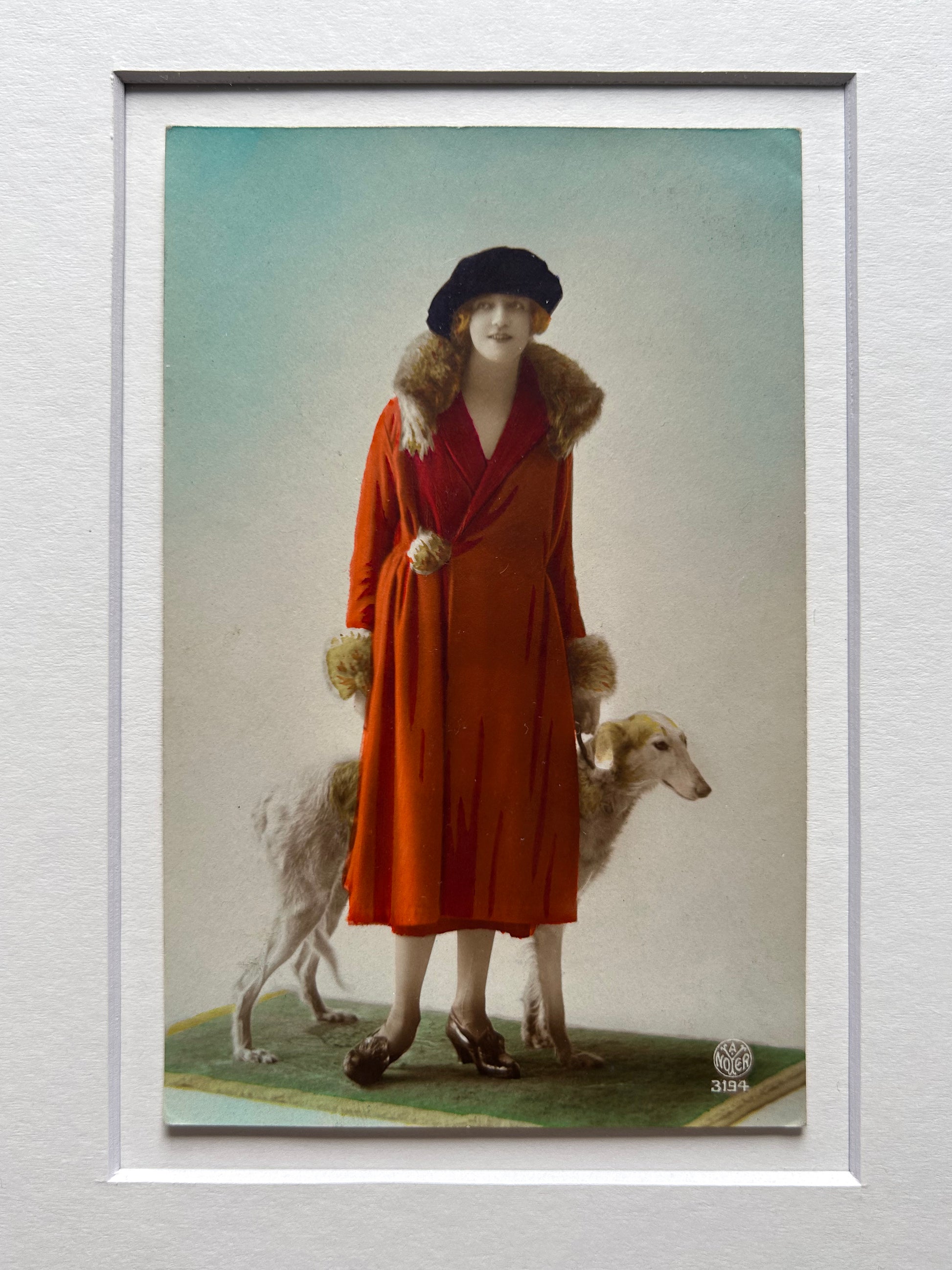 Framed 1920s Fashion Postcard with a poised female model in a fur-trimmed orange coat and black beret, standing confidently beside a Borzoi dog in a handmade Jatoba Wood Frame
