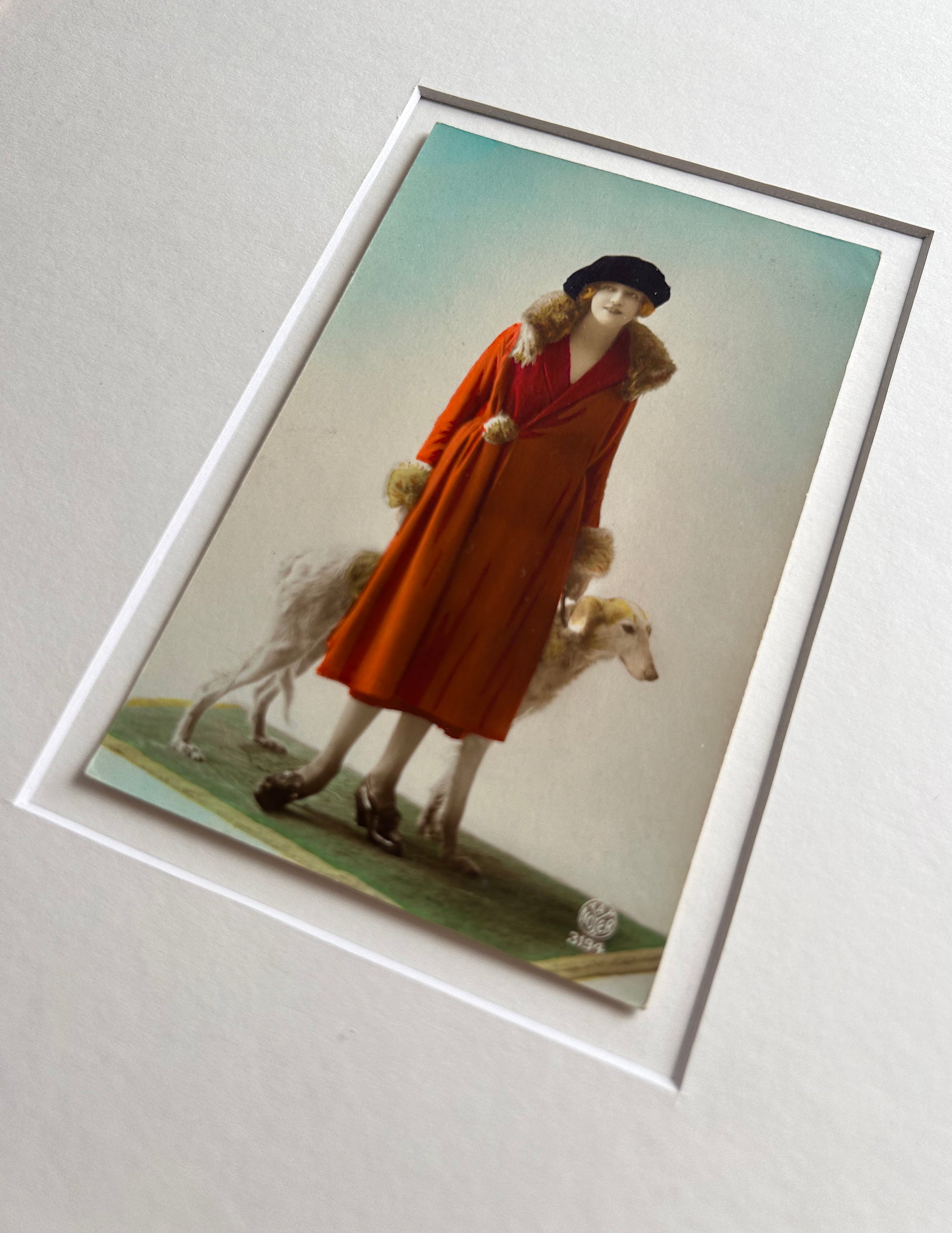 Framed 1920s Fashion Postcard with a poised female model in a fur-trimmed orange coat and black beret, standing confidently beside a Borzoi dog in a handmade Jatoba Wood Frame