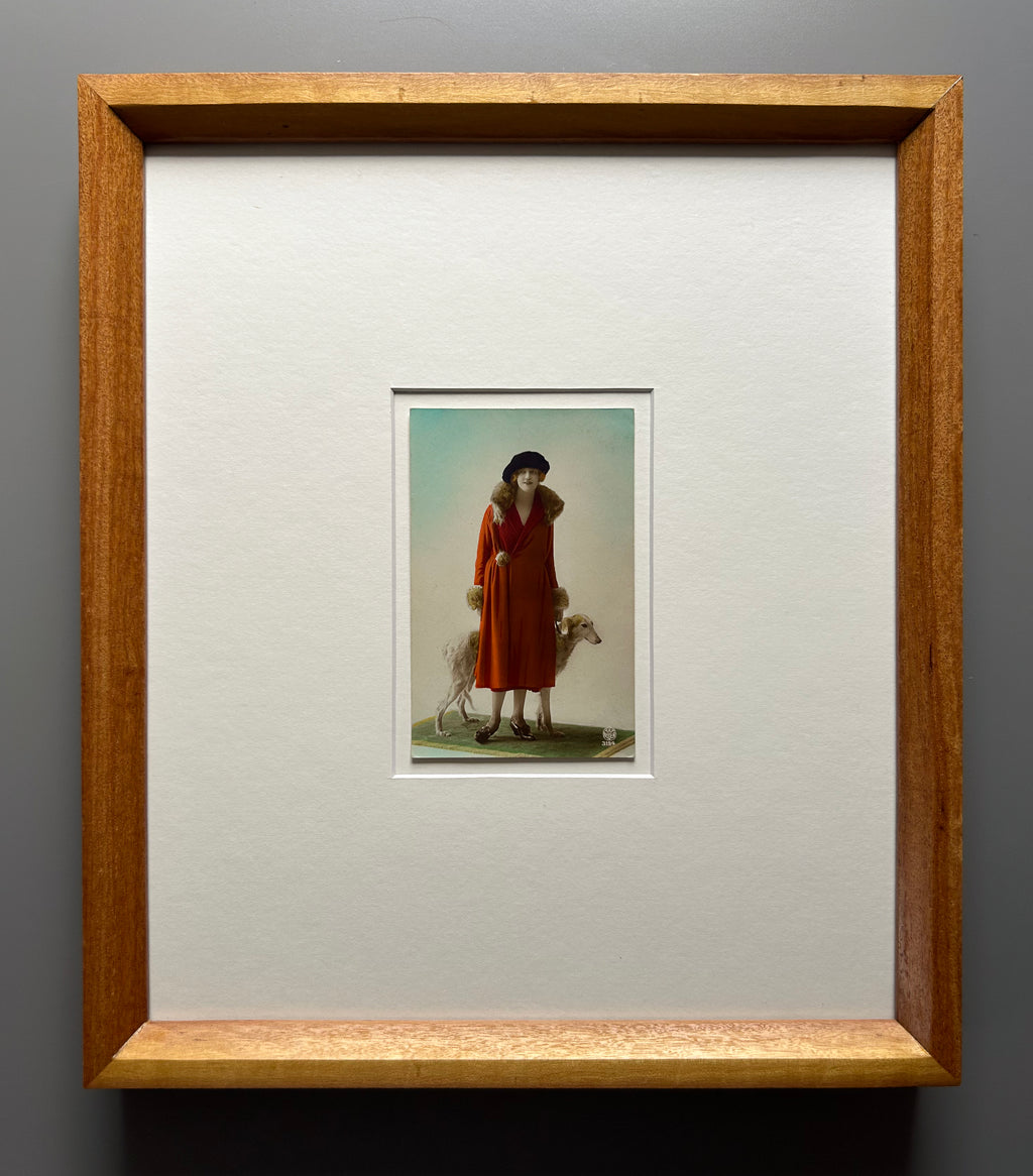 Framed 1920s Fashion Postcard with a poised female model in a fur-trimmed orange coat and black beret, standing confidently beside a Borzoi dog in a handmade Jatoba Wood Frame