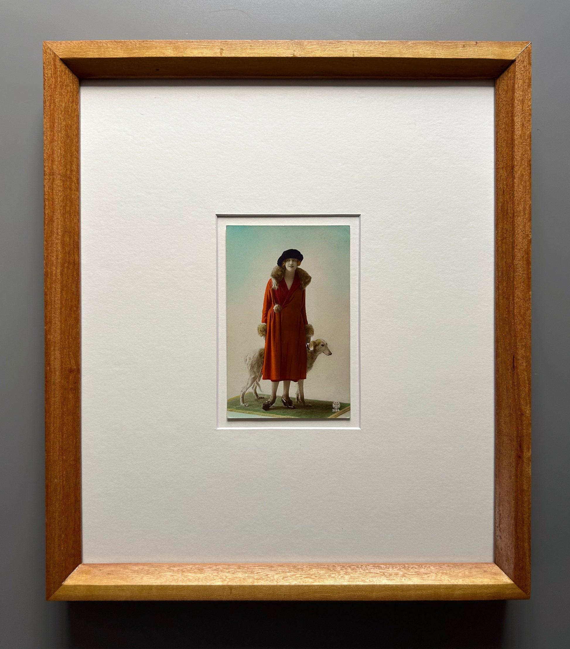 Framed 1920s Fashion Postcard with a poised female model in a fur-trimmed orange coat and black beret, standing confidently beside a Borzoi dog in a handmade Jatoba Wood Frame
