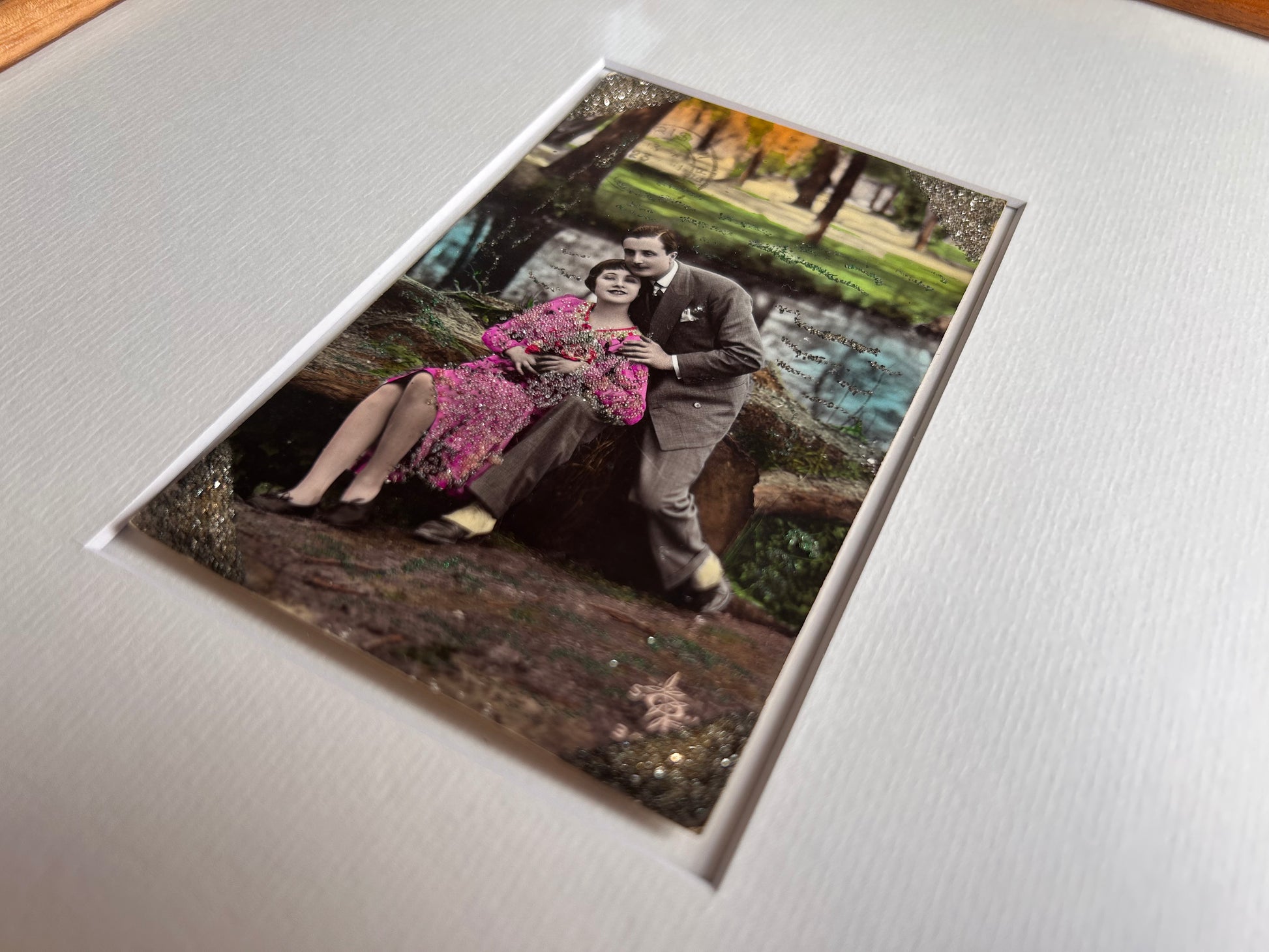 Starts with a great story - Framed 1920s Hand-Tinted and glittered Postcard featuring a tender couple’s embrace in a park – Vintage Romantic Art in Tigerwood Frame