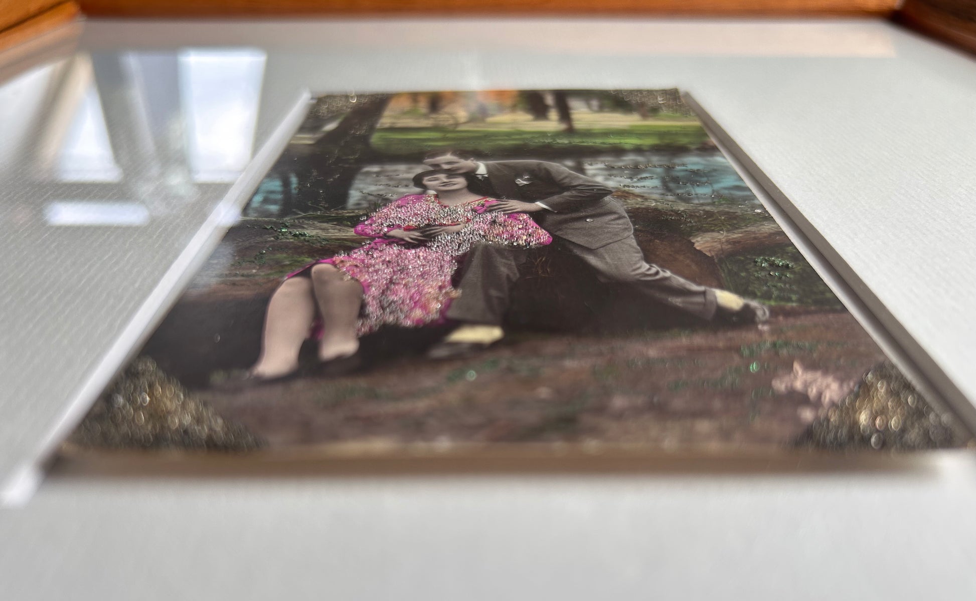 Starts with a great story - Framed 1920s Hand-Tinted and glittered Postcard featuring a tender couple’s embrace in a park – Vintage Romantic Art in Tigerwood Frame