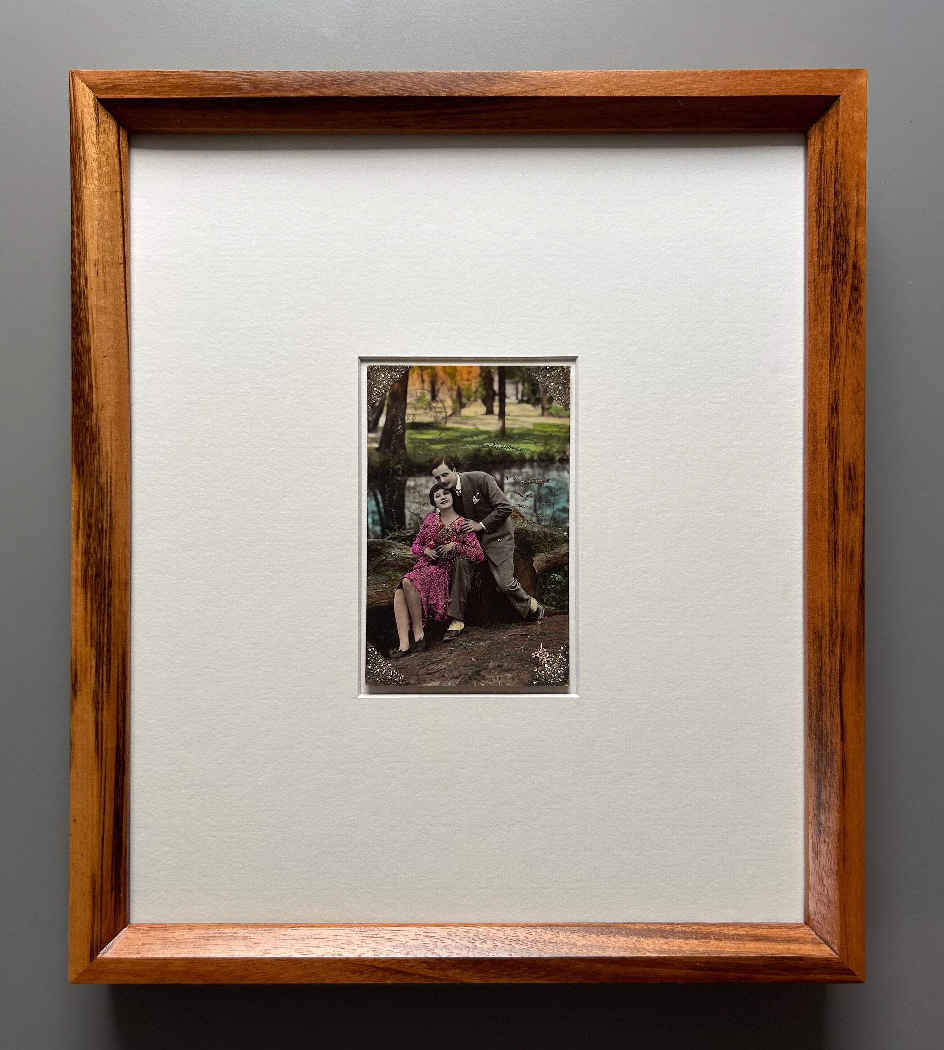 Starts with a great story - Framed 1920s Hand-Tinted and glittered Postcard featuring a tender couple’s embrace in a park – Vintage Romantic Art in Tigerwood Frame